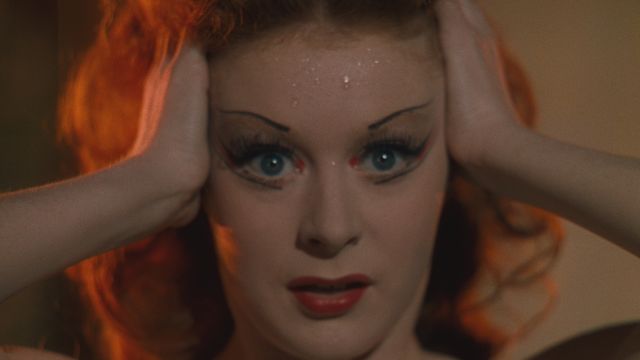 Closeup of woman wearing thin, angular strokes of eyeliner holding her head