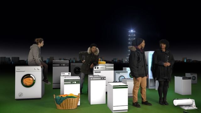 Four people stand among several washing machines in front of a night skyline