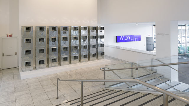 Four rows of silver air conditioners stand stacked on top of each other in a museum lobby. 