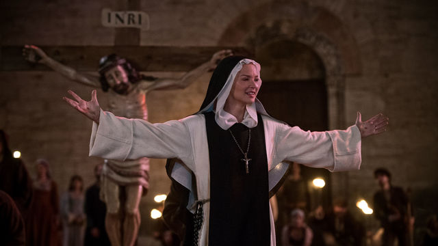 Still from the film "Benedetta" (2021), showing a nun with outstretched arms in front of a triumphal cross