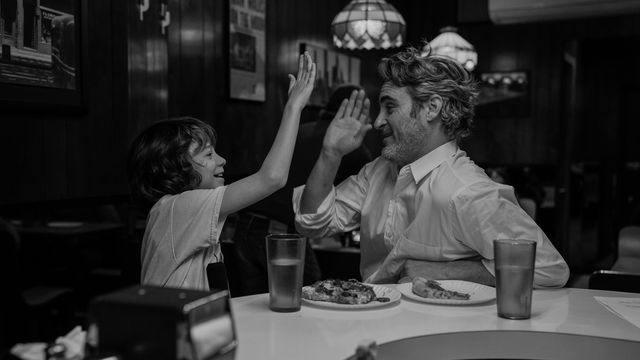 A man and a child sit at a table in a restaurant, giving each other a high five.