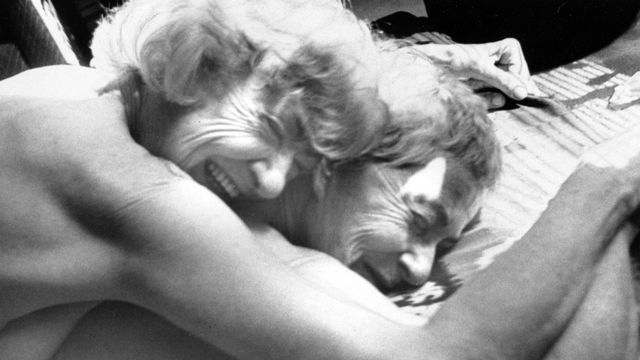 Still from the film "Nitrate Kisses" (1992), showing two naked women lying face down, one on top of the other, both smiling.