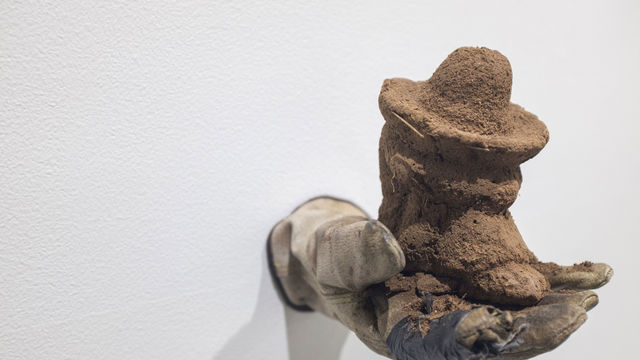 Sculpture of a gloved hand holding an object made of soil and birdseed.