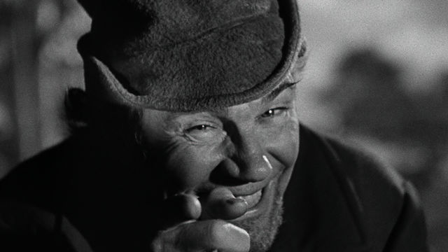 A man in a hat points at the camera.