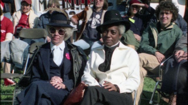 Several people sit on a green lawn in chairs. 