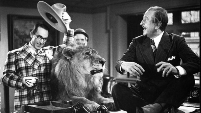 Three men surround a desk that has a lion on top of it.