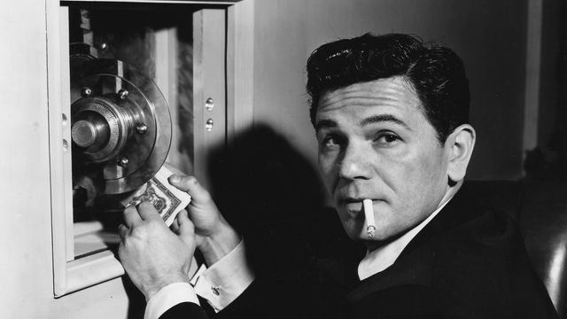 A man smoking a cigarette holding a stack of bills.