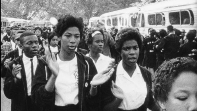 A group of people march next to a set of buses.