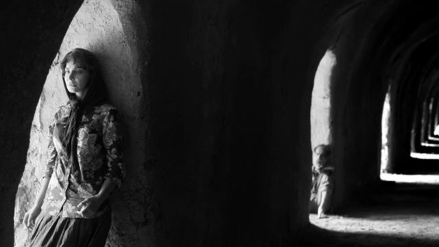 A man and a woman stand in dark corridors.