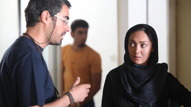 A man with glasses speaks to a woman in a hijab. 