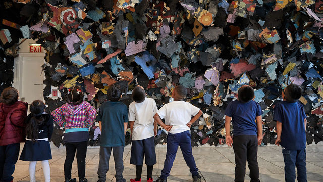 A line of children, seen from behind, looking up at a large artwork