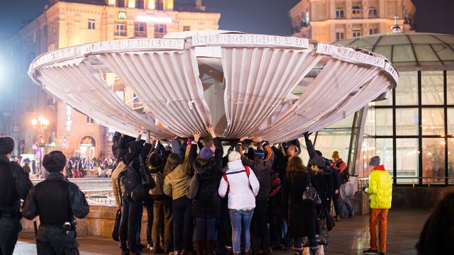 Several people attempt to touch a tall trumpeting structure in the center of a fountain.