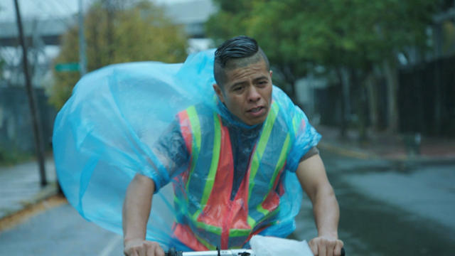 Man wearing poncho bikes in rain.