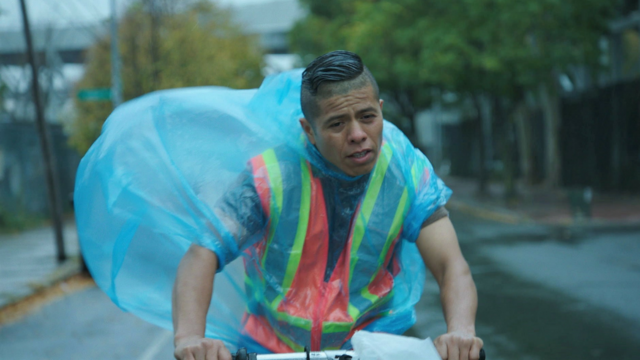 Man wearing poncho bikes in rain. 