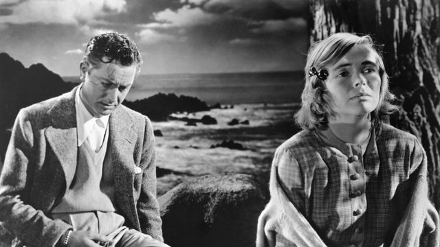 Man and a woman sit in front of an ocean background.