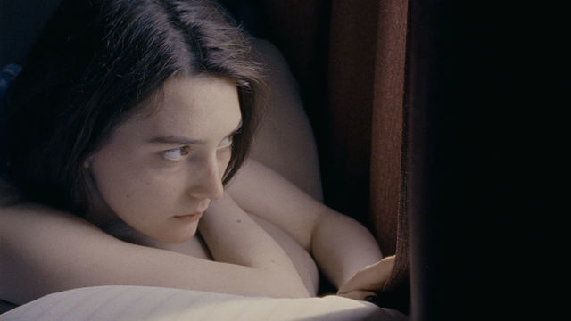A woman lies on a bed and looks out a window.