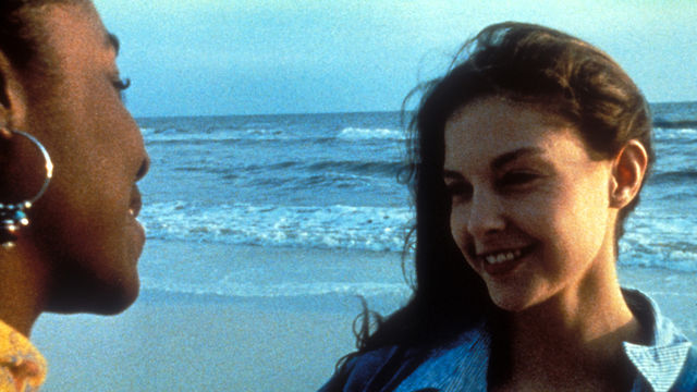 Two women speak to each other in front of the ocean.