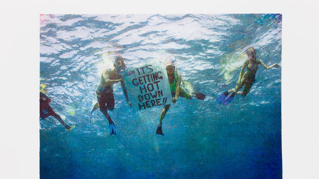 An underwater image looking up at a group of four activists snorkeling, two holding a sign that reads "IT'S GETTING HOT DOWN HERE!!"