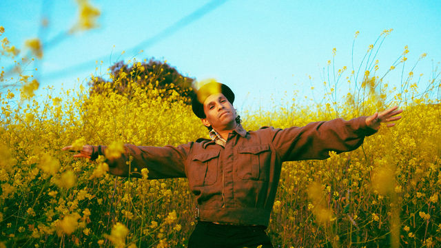 The musician Pachyman standing in a yellow field with his arms spread wide