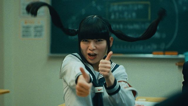 A girl with pigtails in school holds thumbs up.