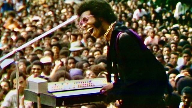 Still from the documentary film "Summer of Soul" (2021) showing Sly Stone performing in front of a large crowd