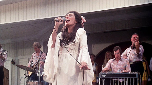 A woman in a white dress singing on stage in a still from the film "Nashville" (1975)