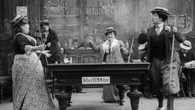 A group of women stand around a pool table.