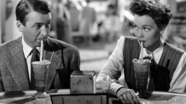 A man and woman make eye contact while sipping on milk shakes. 