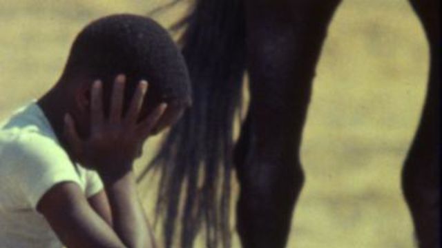 Boy holds head in hands. Part of a horse shows in the background.