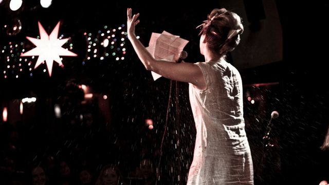 Woman singing from sheet music with a black background and starlights