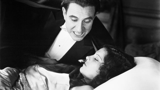 Masculine vampire lurks next to the bed of a sleeping woman