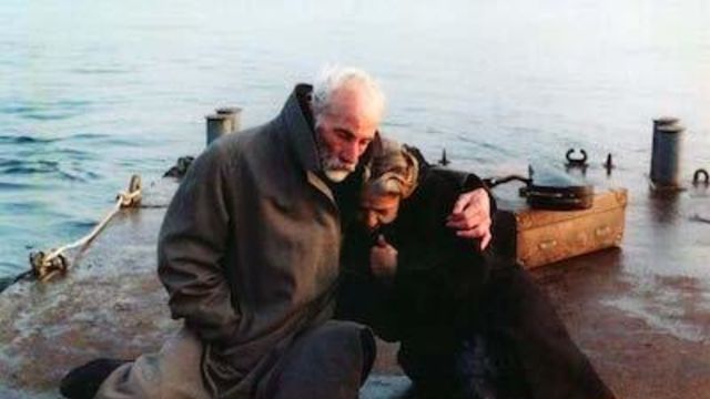 Man holds woman close while they sit by the ocean