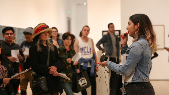 A tour guide speaks into a microphone as a group of visitors listen