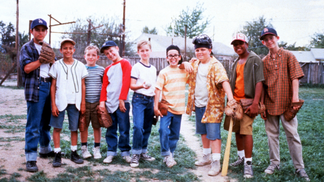 A group of boys stand on a deteriorating grass field in old baseball gear