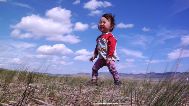 A smiling baby stands in a field