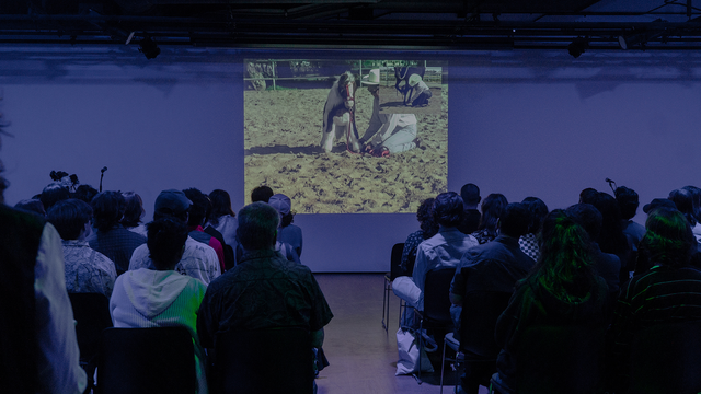 Audience sits in purple dim lit room watching a projected film