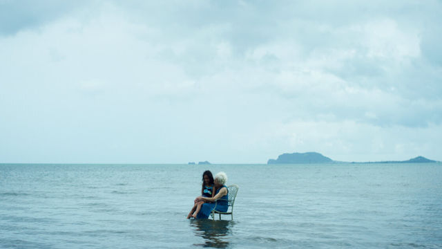 woman and child sit in lawn chair floating in ocean