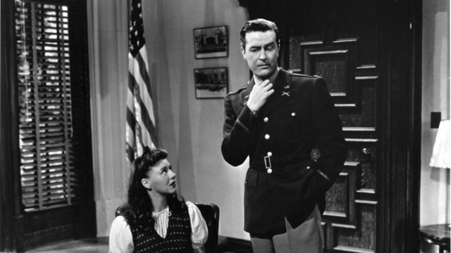 Woman looks up at man in black and white government office