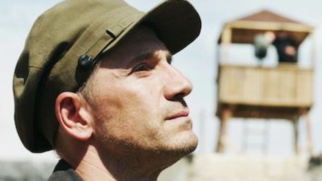 Still from Amerikatsi showing a man in closeup with a guard tower in soft focus behind him