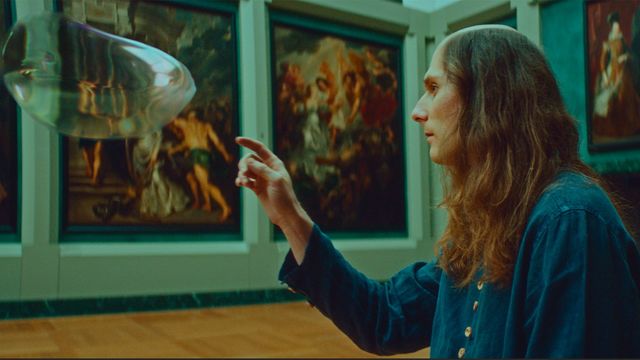 A man in a museum gallery reaching out to pop a big bubble.