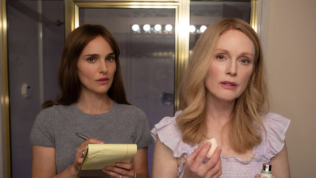 Natalie Portman and Julianne Moore stand in a bathroom, Moore putting on makeup, Portman taking notes