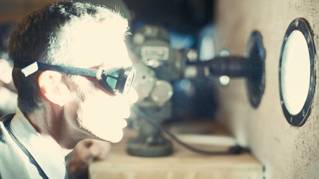 A man looking through a porthole, wearing goggles