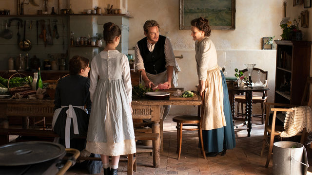 Four people in old garb stand around a dining table