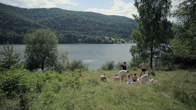 A family sits in a field by a body of water