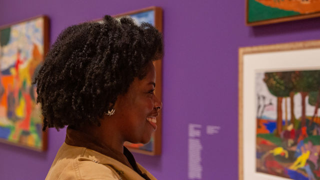 A smiling Black woman looks at art in a bright gallery