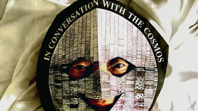 Photo of David Medalla wearing a mask that reads "in conversation with the cosmos"