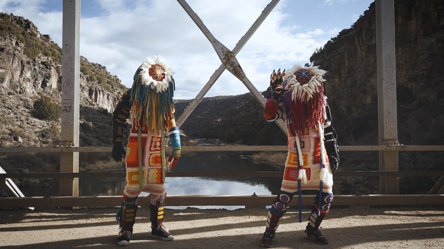 Two figures in colorful costumes standing on a bridge