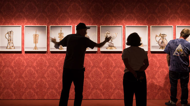 A man, viewed in silhouette, stands in front of a wall of framed artworks