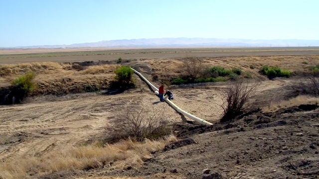 Two men work on a pipeline in a desert landscape