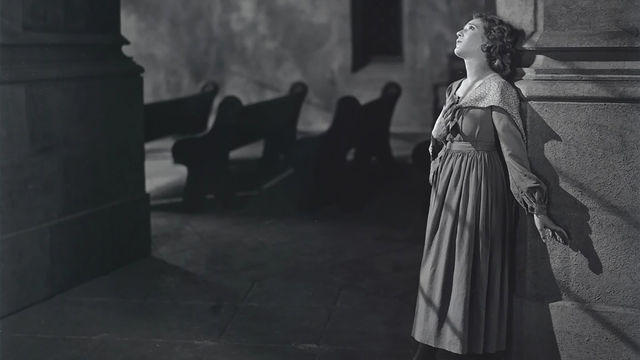 Mary Pickford leans against a wall, looking up at the light
